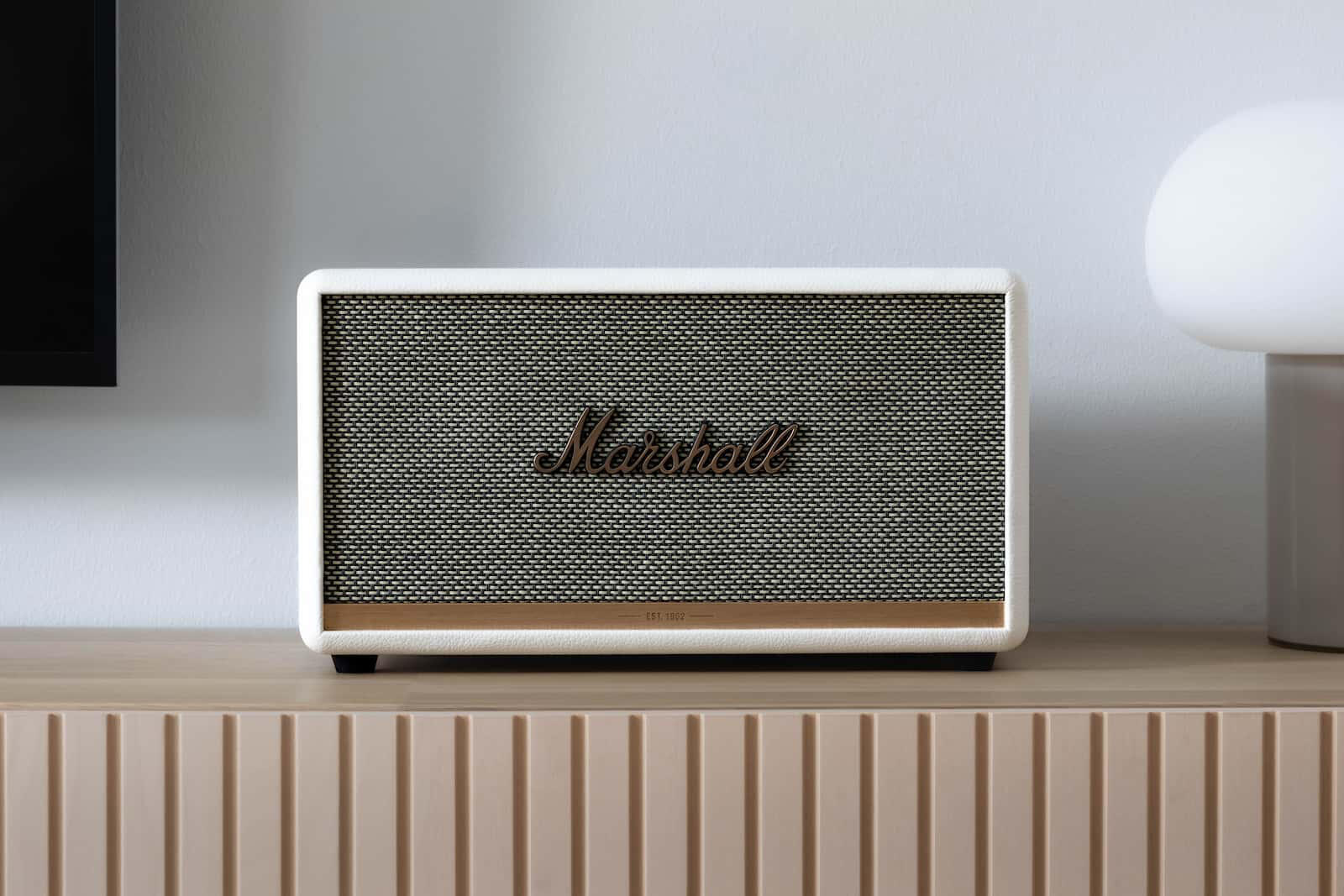 Mashall Stanmore II -kaiutin kuvattuna suoraan edestä. Vieressä lamppu ja tv.