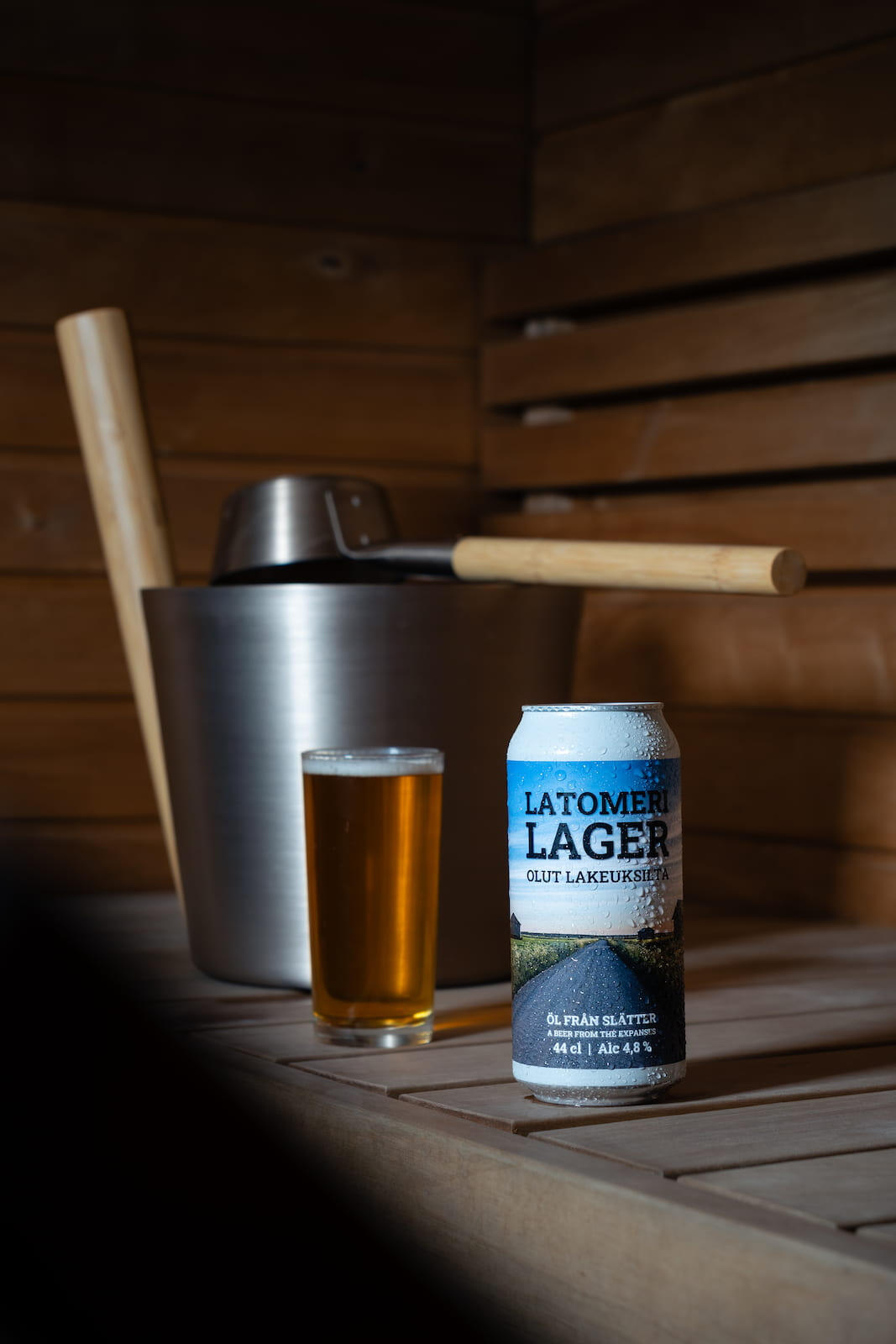Latomeri Lager tölkki saunan lauteilla, taustalla kiulu ja olutlasi.