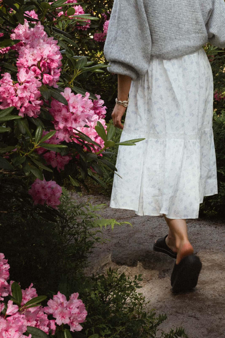 Malli on selin kameraan ja kävelee alppiruusujen ympäröimää polkua metsässä.