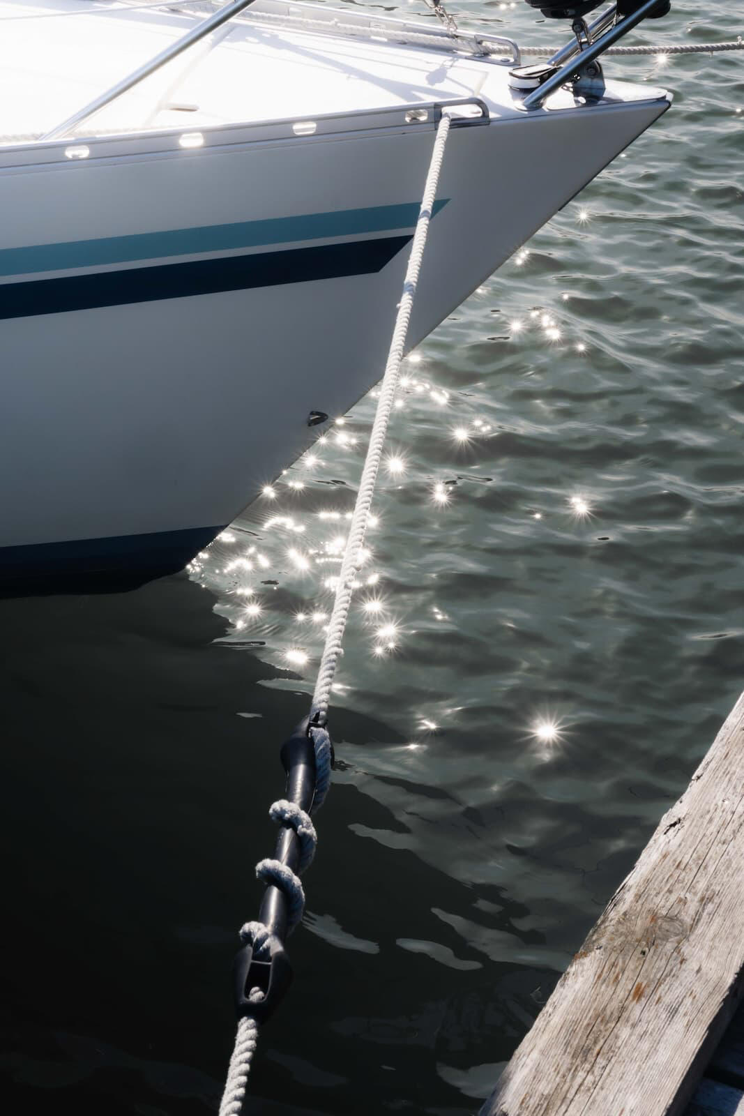 Kuva veneen keulasta, kiinnitysköysistä ja auringon kimaltelusta vedenpinnalla.