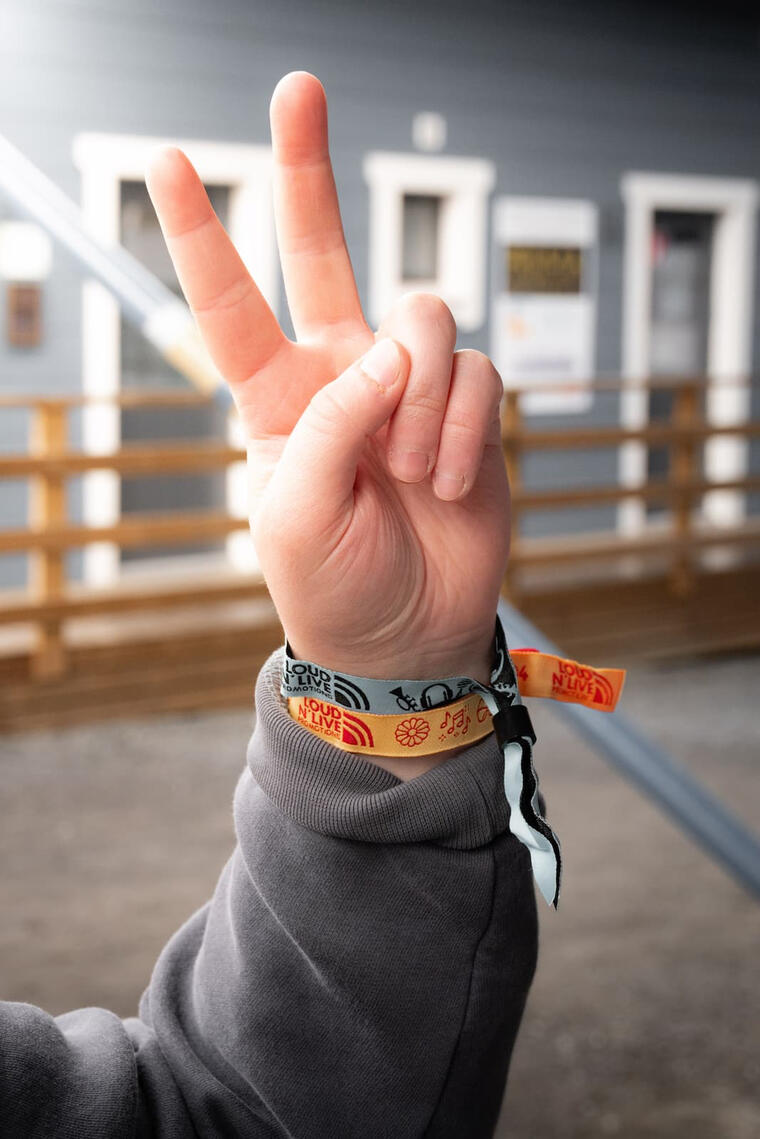 Kuvassa käsi tekee "peace" merkin ja ranteessa on kaksi festivaalien ranneketta.