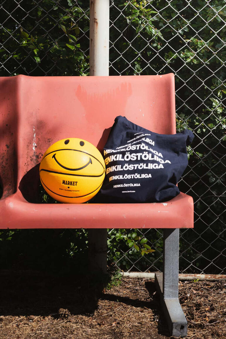 Oranssi koripallo ja sininen kangaskassi punaisella penkillö koripallokentällä.