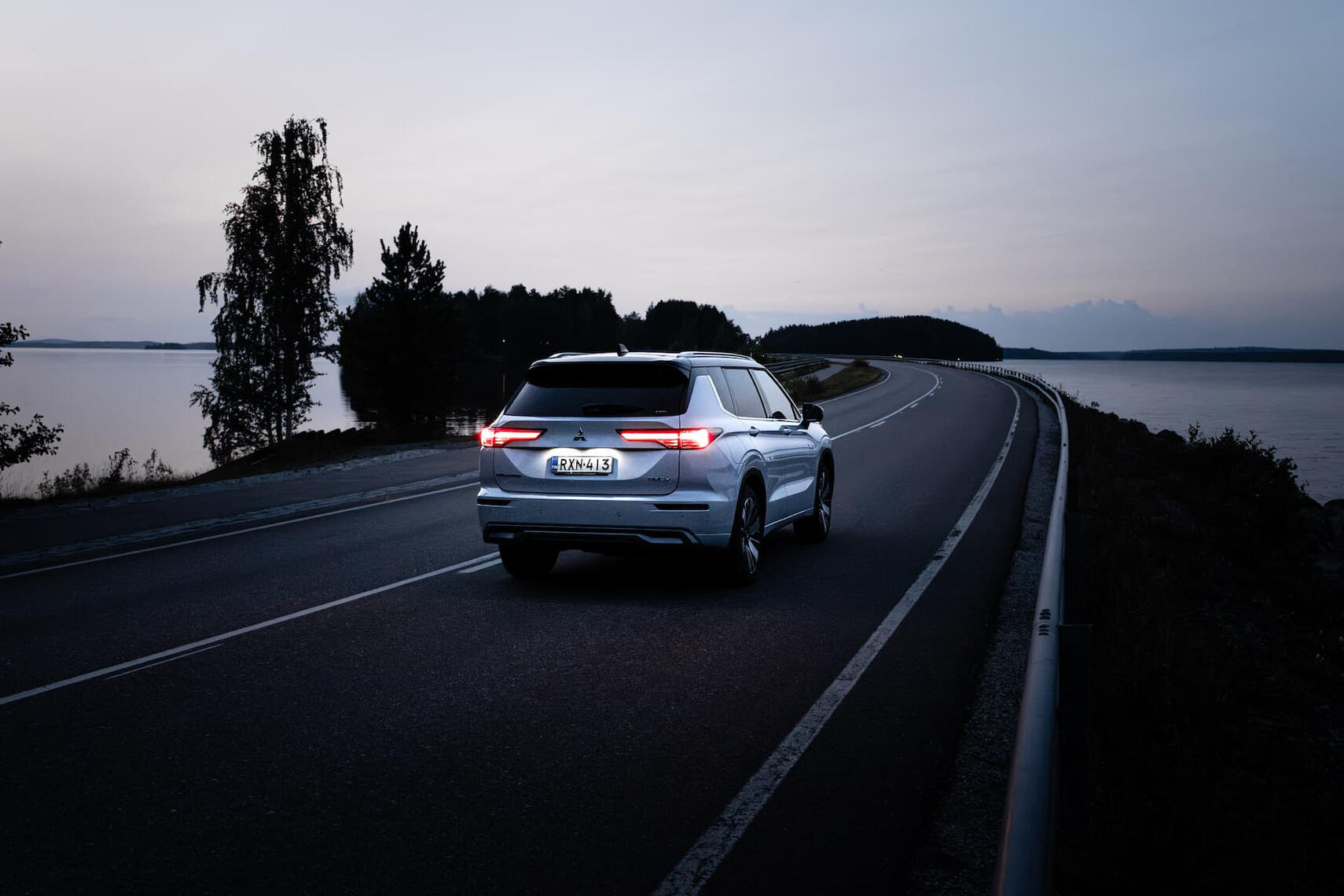 Mitsubishi Outlander takaviistosta kuvattuna iltahämärässä keskellä suomalaista järvimaisemaa.