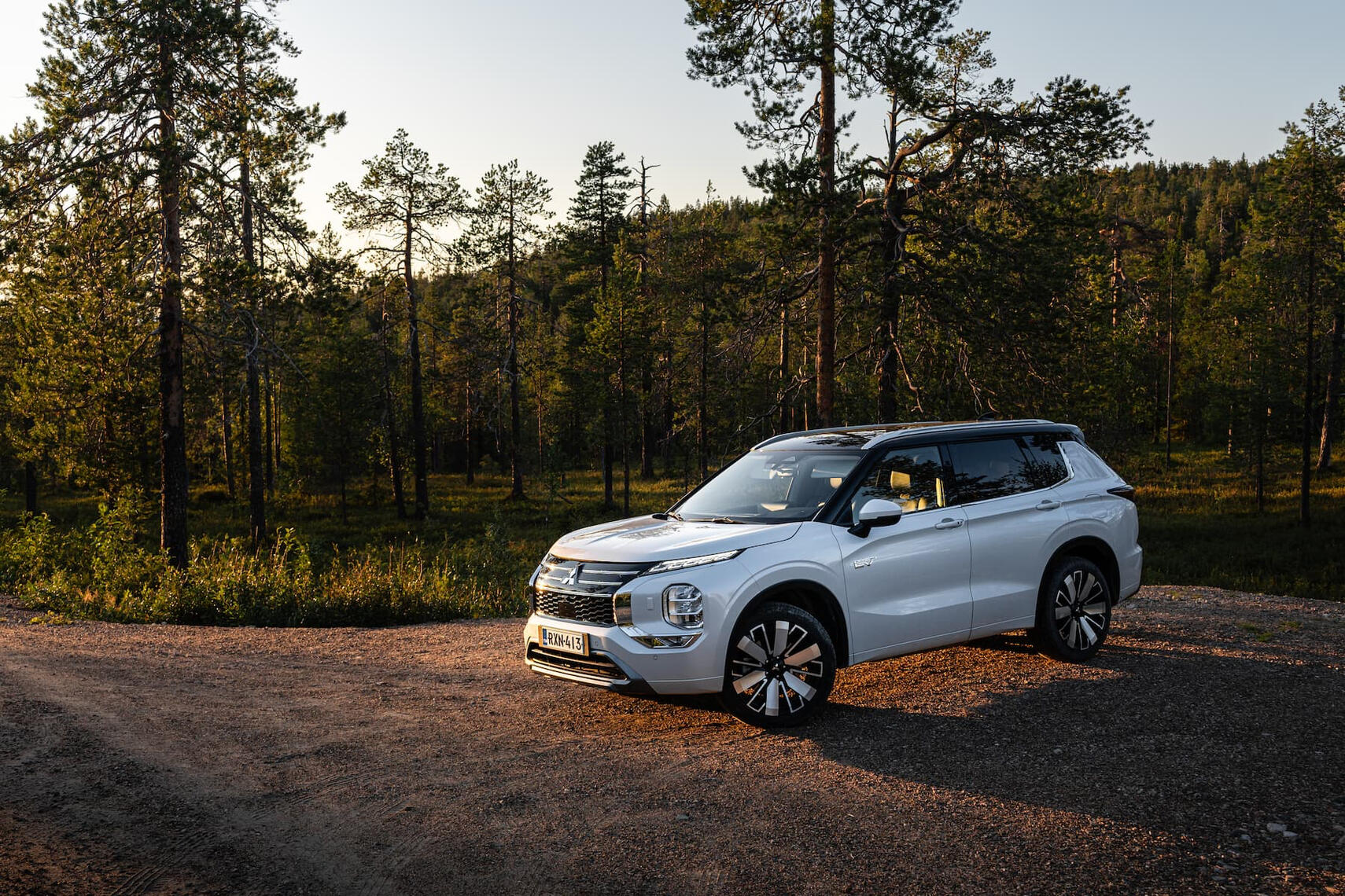 Mitsubishi Oulander etuviistosta kuvattuna havupuiden edessä auringonlaskun aikaan.