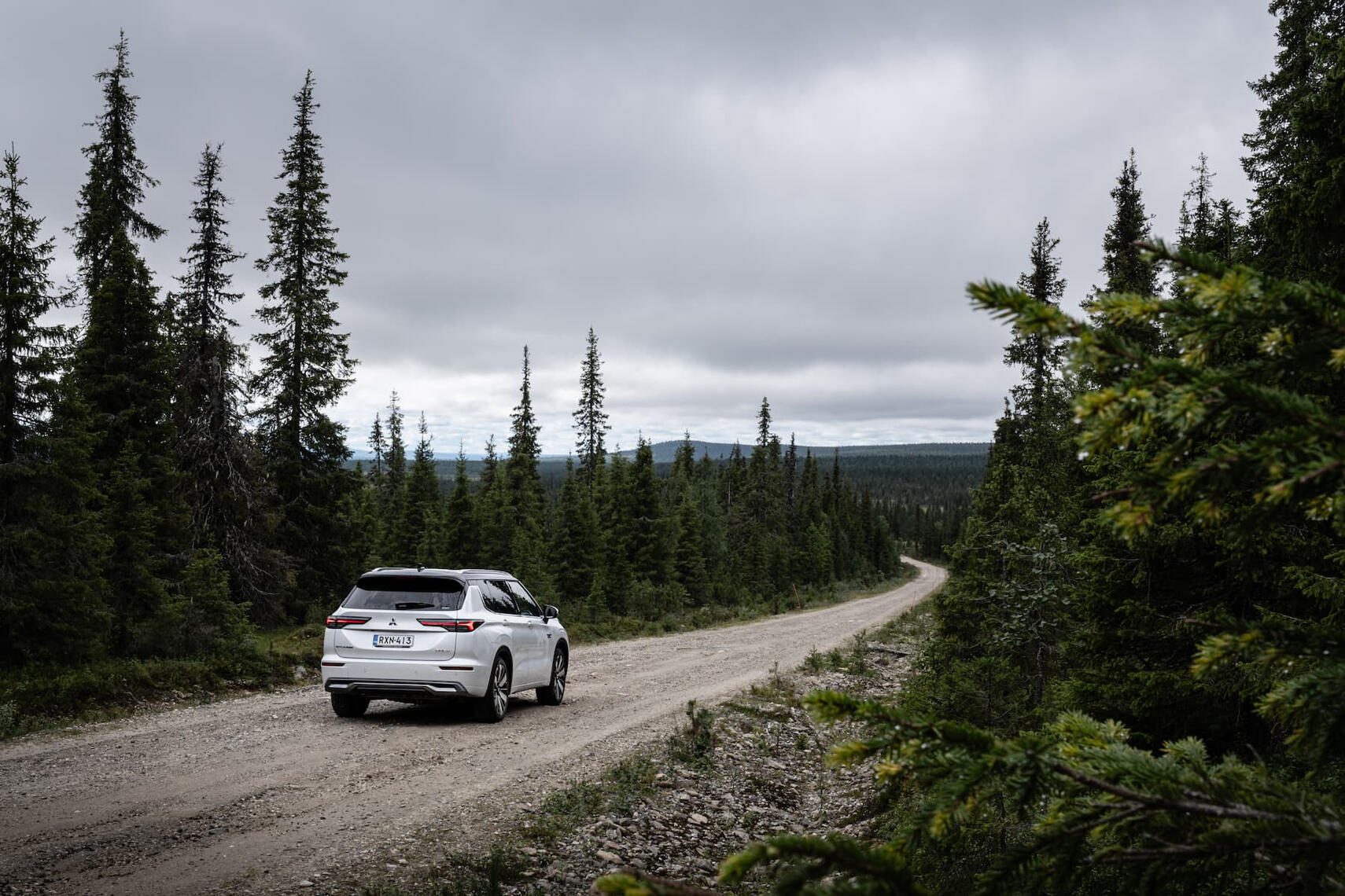 Mitsubishi Outlander takaviistosta kuvattuna, edessään pitkä ja mutkainen hiekkatie lapin havumetsässä.
