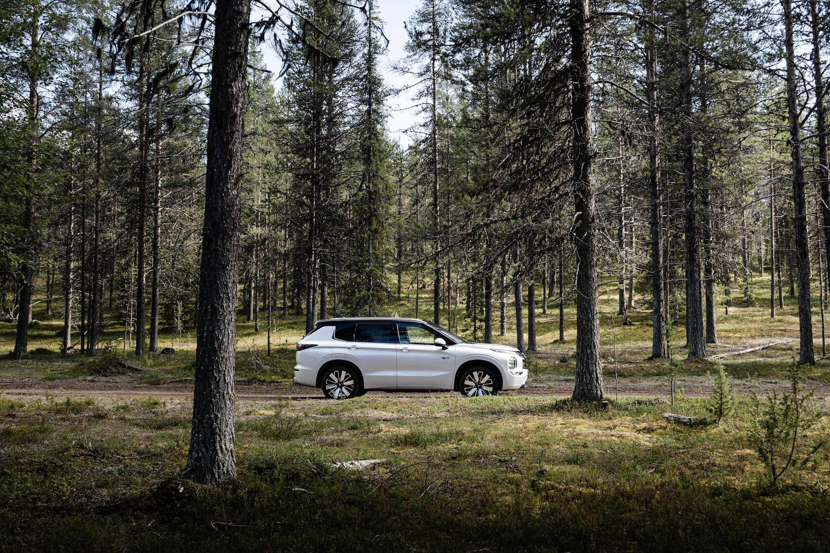 Mitsubishi Outlander sivulta kuvattuna havumetsän keskellä.