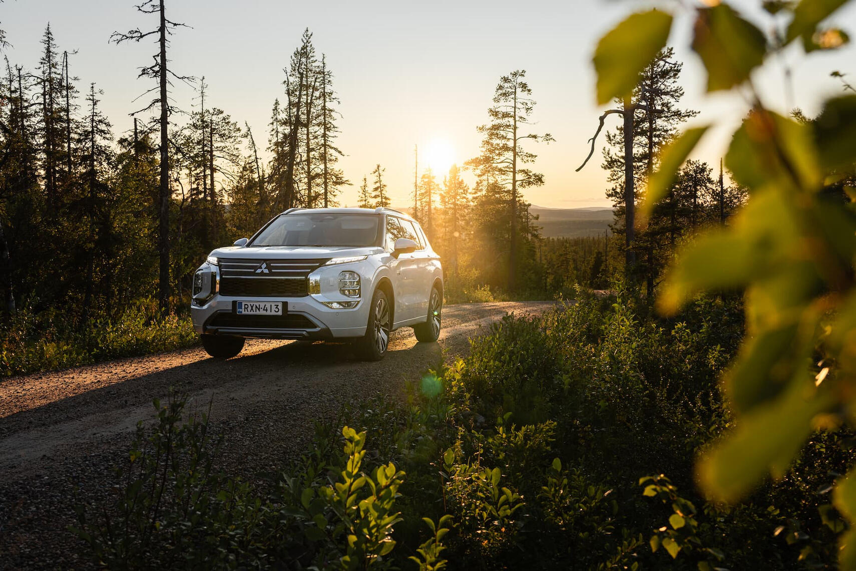 Mitsubishi Outlander edestä kuvattuna tunturin päällä auringonlaskun aikaan, taustalla tunturimaisema.