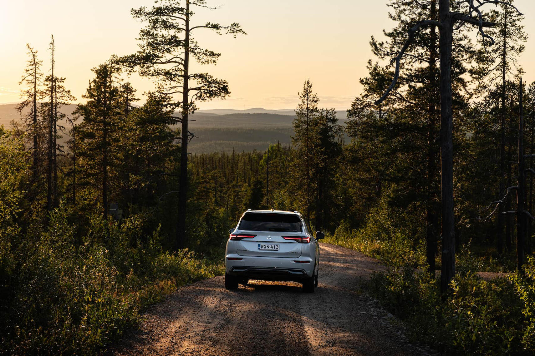 Mitsubishi Outlander takaa kuvattuna, edessä pitkälle näkyvä tunturimaisema auringonlaskun aikaa.