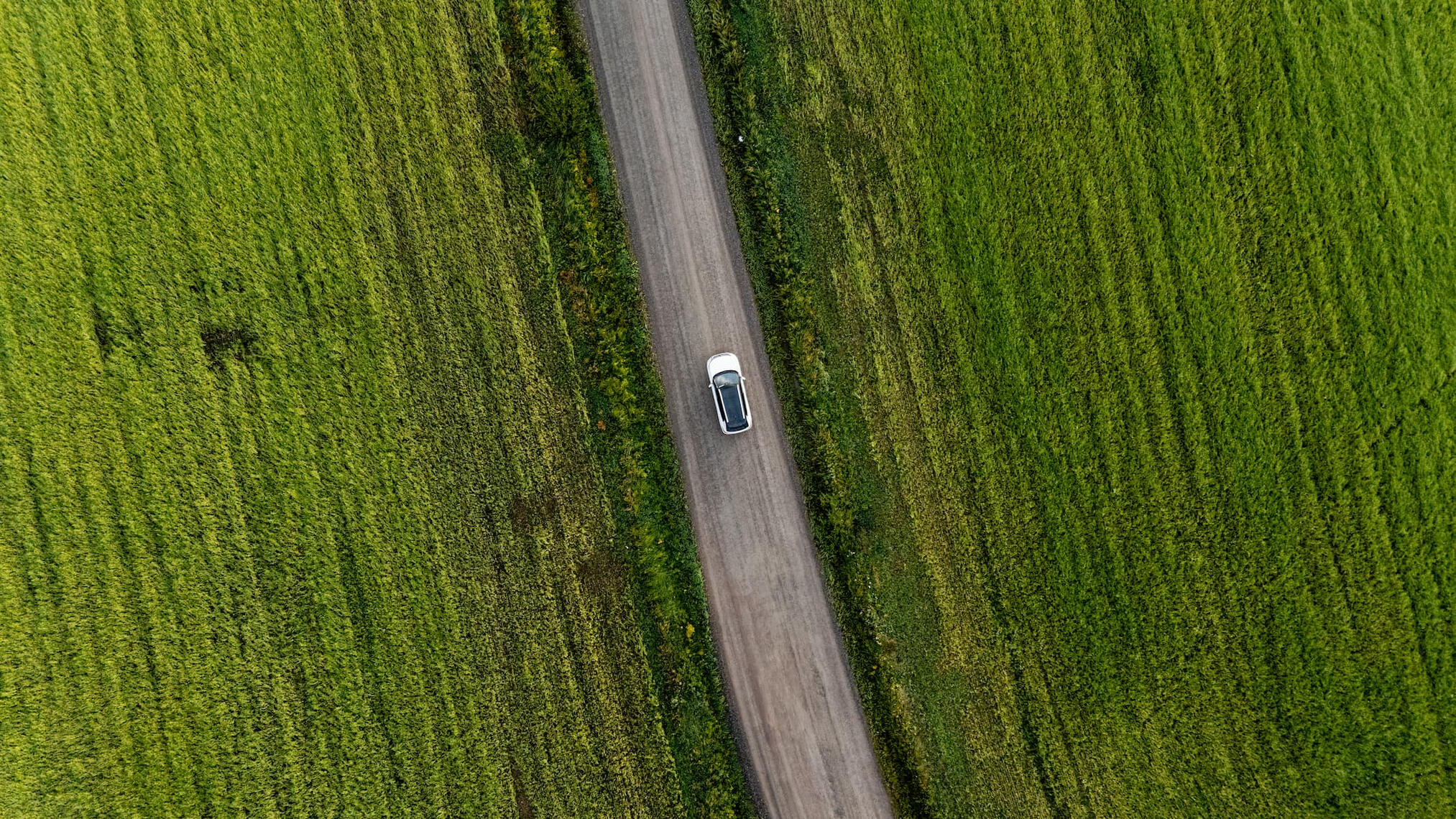 Mitsubishi Outlander suoraan ylhäältä dronella kuvattuna peltojen ympäröimällä hiekkatiellä.